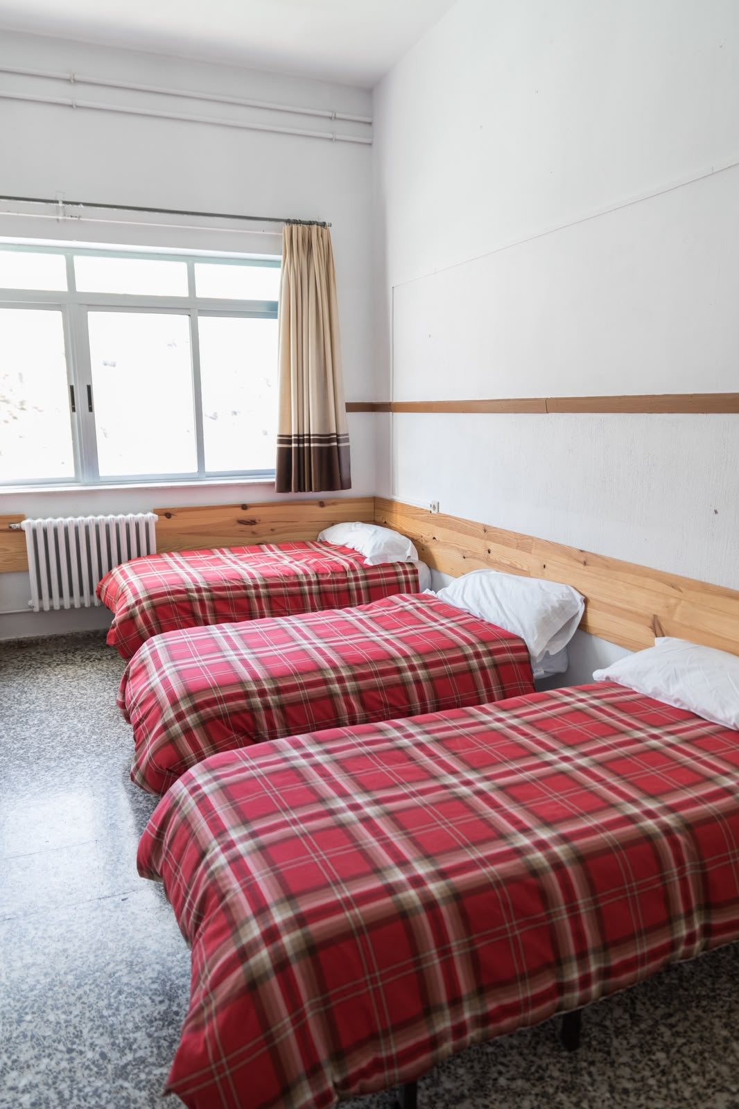 Habitación con tres camas y colchas de cuadros rojos