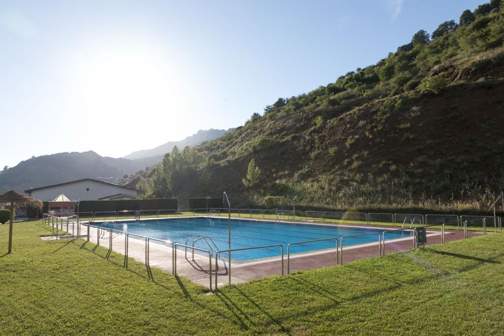 Piscina al aire libre rodeada de césped al pie de la montaña
